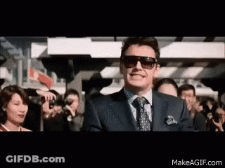 A Man Wearing Sunglasses And A Suit Is Standing In Front Of A Crowd Of People . GIF