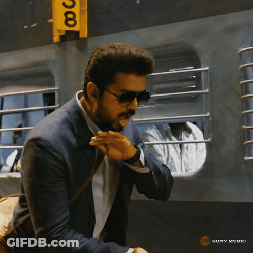 A Man Wearing Sunglasses And A Suit Is Standing In Front Of A Yellow Sign That Says Sony Music GIF