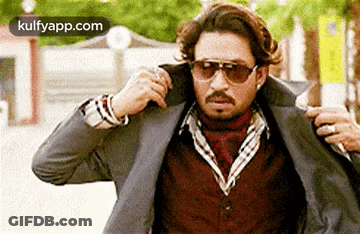 A Man Wearing Sunglasses And A Suit Jacket Is Being Helped By Another Man . GIF