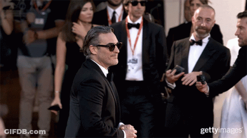 A Man Wearing Sunglasses And A Tuxedo Is Being Escorted By A Group Of Men GIF