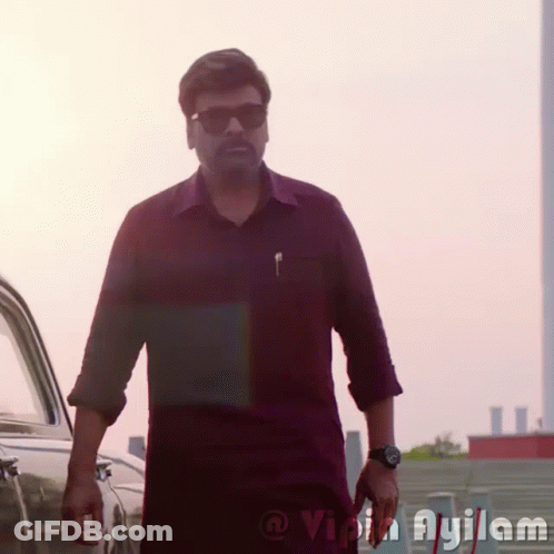 A Man Wearing Sunglasses And A Watch Is Standing In Front Of A Car With The Word Ayilam On The Bottom Right GIF