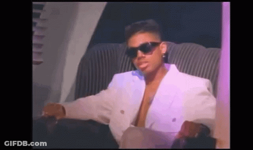 A Man Wearing Sunglasses And A White Jacket Is Sitting In A Chair . GIF
