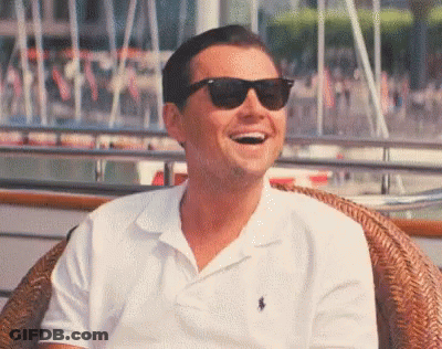 A Man Wearing Sunglasses And A White Polo Shirt Is Sitting In A Chair And Laughing . GIF