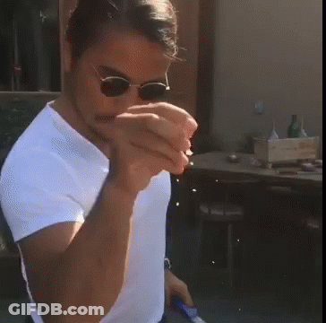 A Man Wearing Sunglasses And A White Shirt Holds Something In His Hands GIF
