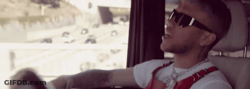 A Man Wearing Sunglasses And A White Shirt Is Driving A Car GIF