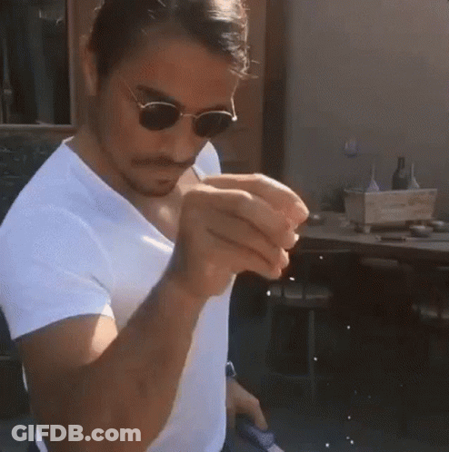 A Man Wearing Sunglasses And A White Shirt Is Holding A Piece Of Food In His Hand . GIF