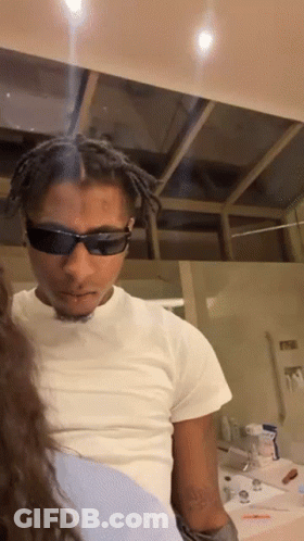 A Man Wearing Sunglasses And A White Shirt Is Looking At A Woman GIF