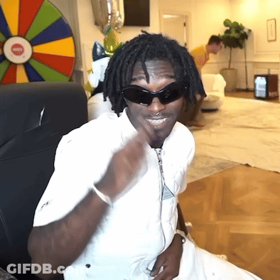 A Man Wearing Sunglasses And A White Shirt Is Sitting In Front Of A Wheel Of Fortune GIF