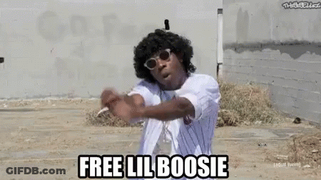 A Man Wearing Sunglasses And A White Shirt Is Standing In A Dirt Field And Says `` Free Lil Boosi '' . GIF