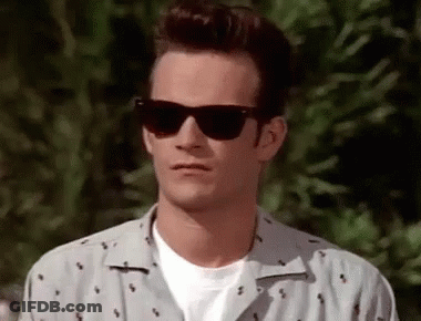 A Man Wearing Sunglasses And A White Shirt Is Standing In Front Of A Tree . GIF