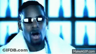 A Man Wearing Sunglasses And A White Shirt Is Standing In Front Of A Wall With A Blue Light Behind Him . GIF