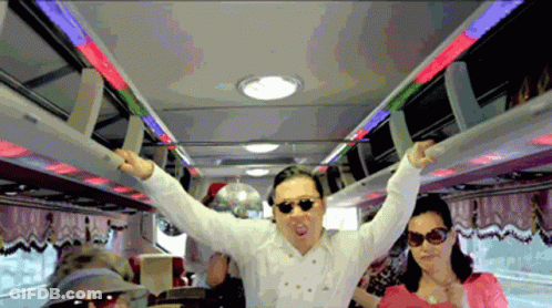 A Man Wearing Sunglasses And A White Shirt Stands In A Bus With His Arms Outstretched GIF