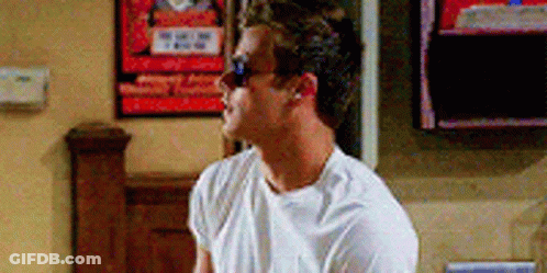 A Man Wearing Sunglasses And A White T-Shirt Is Sitting In Front Of A Tv . GIF