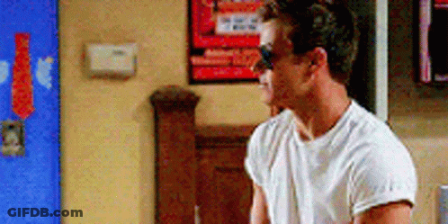 A Man Wearing Sunglasses And A White T-Shirt Is Standing In A Room . GIF
