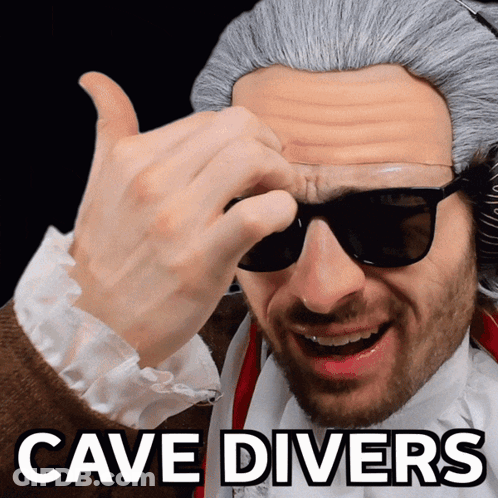 A Man Wearing Sunglasses And A Wig With The Words Cave Divers Above Him GIF