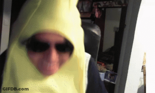 A Man Wearing Sunglasses And A Yellow Hood Is Standing In A Room GIF