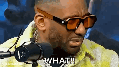 A Man Wearing Sunglasses And A Yellow Jacket Is Sitting In Front Of A Microphone And Saying What . GIF