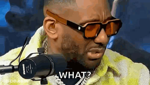 A Man Wearing Sunglasses And A Yellow Jacket Is Standing In Front Of A Microphone And Asking What . GIF
