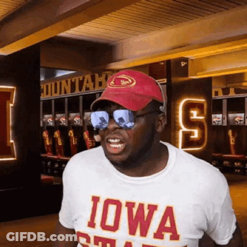 A Man Wearing Sunglasses And An Iowa Shirt Stands In A Locker Room . GIF