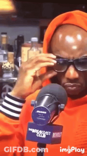 A Man Wearing Sunglasses And An Orange Hoodie Stands In Front Of A Breakfast Club Microphone GIF