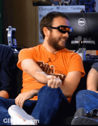 A Man Wearing Sunglasses And An Orange Shirt Sitting In Front Of A Dell Monitor GIF