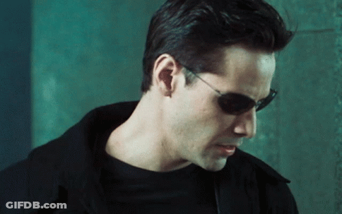 A Man Wearing Sunglasses And Ear Buds Looks Down GIF