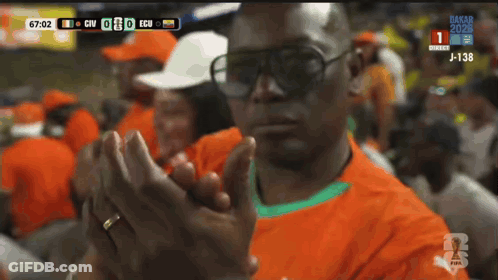 A Man Wearing Sunglasses Applauds During A Soccer Match GIF
