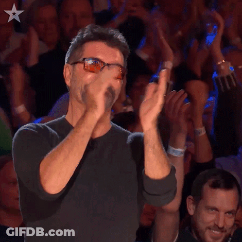 A Man Wearing Sunglasses Applauds In Front Of A Crowd Of People GIF