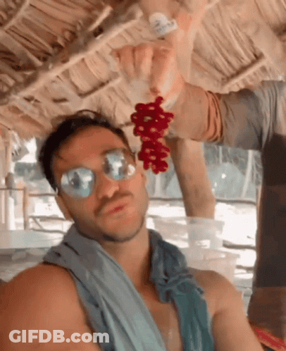 A Man Wearing Sunglasses Holds A Bunch Of Red Grapes In His Hand GIF