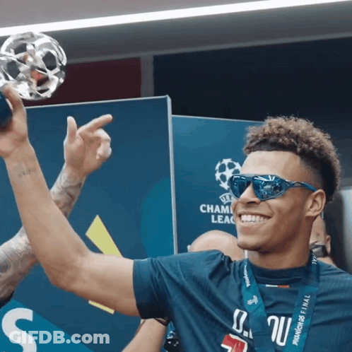 A Man Wearing Sunglasses Holds Up A Trophy With The Word Champions On It GIF