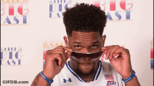 A Man Wearing Sunglasses In Front Of A Big East Banner GIF