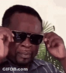 A Man Wearing Sunglasses Is Adjusting His Glasses And Making A Funny Face . GIF