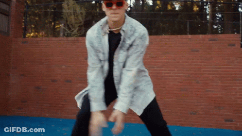 A Man Wearing Sunglasses Is Dancing In Front Of A Red Brick Wall GIF
