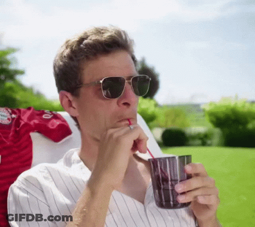 A Man Wearing Sunglasses Is Drinking From A Glass Through A Straw GIF