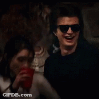 A Man Wearing Sunglasses Is Drinking From A Red Cup While A Woman Looks On . GIF