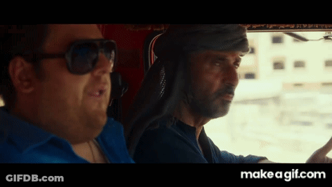 A Man Wearing Sunglasses Is Driving A Car Next To Another Man GIF