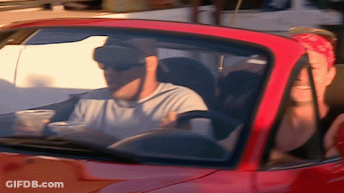 A Man Wearing Sunglasses Is Driving A Red Sports Car GIF