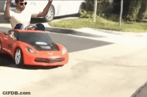 A Man Wearing Sunglasses Is Driving A Red Toy Car GIF