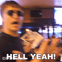 A Man Wearing Sunglasses Is Holding A Box Of Money And Says Hell Yeah GIF