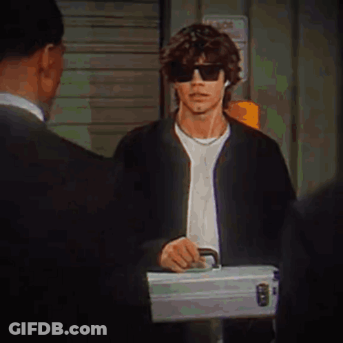 A Man Wearing Sunglasses Is Holding A Briefcase While Talking To A Man In A Suit . GIF