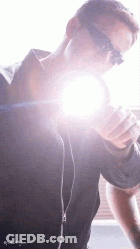 A Man Wearing Sunglasses Is Holding A Flashlight In His Hand GIF