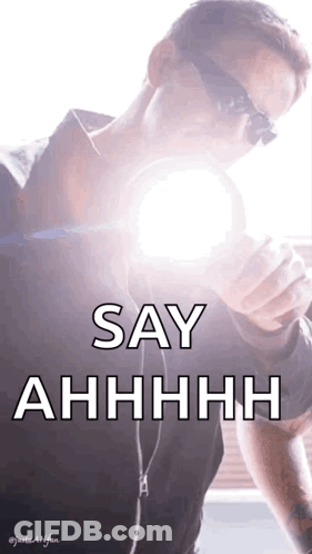 A Man Wearing Sunglasses Is Holding A Light Bulb In His Hand And Says Say Ahhhh GIF