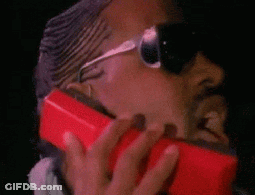 A Man Wearing Sunglasses Is Holding A Red Cell Phone To His Face . GIF
