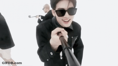 A Man Wearing Sunglasses Is Holding A Stick In His Hand While Standing Next To Another Man . GIF