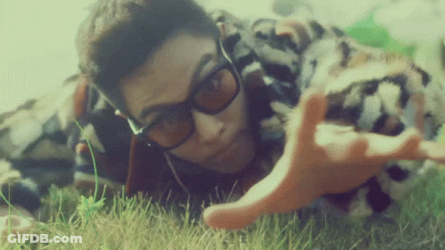 A Man Wearing Sunglasses Is Laying In The Grass With His Hands Outstretched GIF