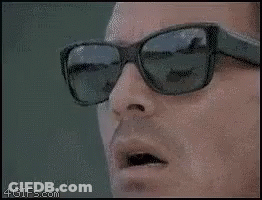 A Man Wearing Sunglasses Is Looking Down At Something . GIF
