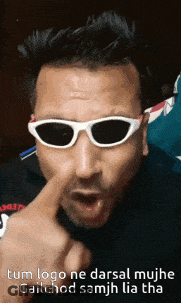 A Man Wearing Sunglasses Is Making A Funny Face With His Finger In His Nose GIF