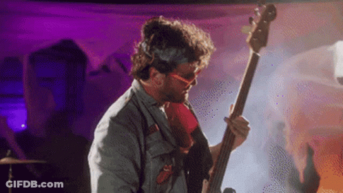 A Man Wearing Sunglasses Is Playing A Bass Guitar GIF