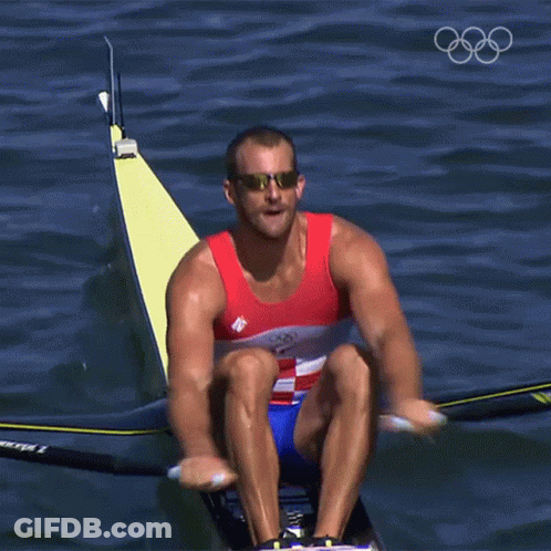 A Man Wearing Sunglasses Is Rowing A Boat In The Water With The Olympic Rings In The Background GIF