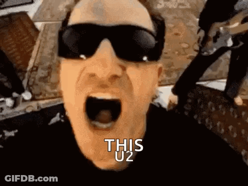 A Man Wearing Sunglasses Is Screaming With His Mouth Wide Open And The Words `` This U2 '' Written On His Face . GIF